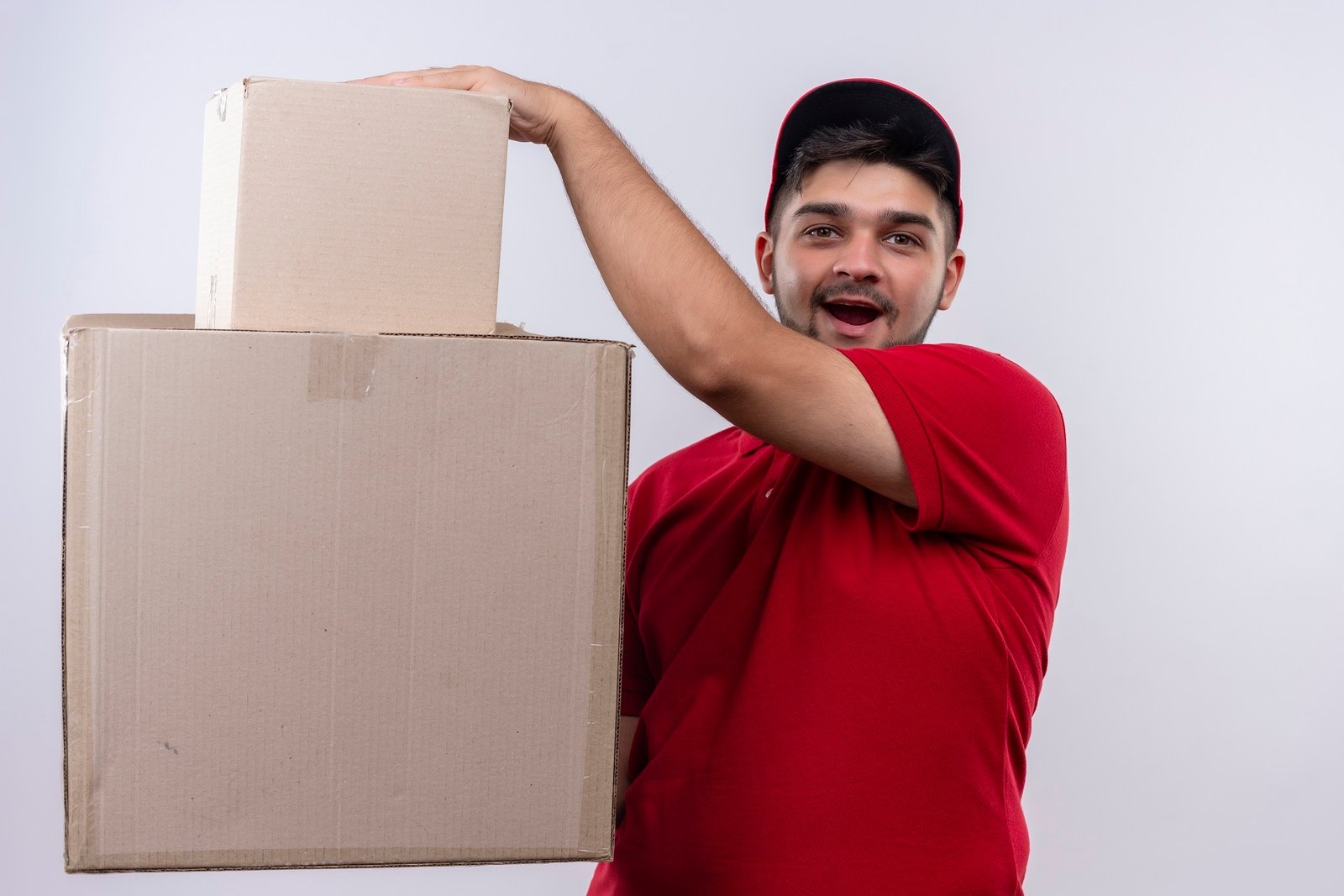 About Us young delivery man in red uniform and cap holding large cardboard boxes looking surprised and amazed standing over white background